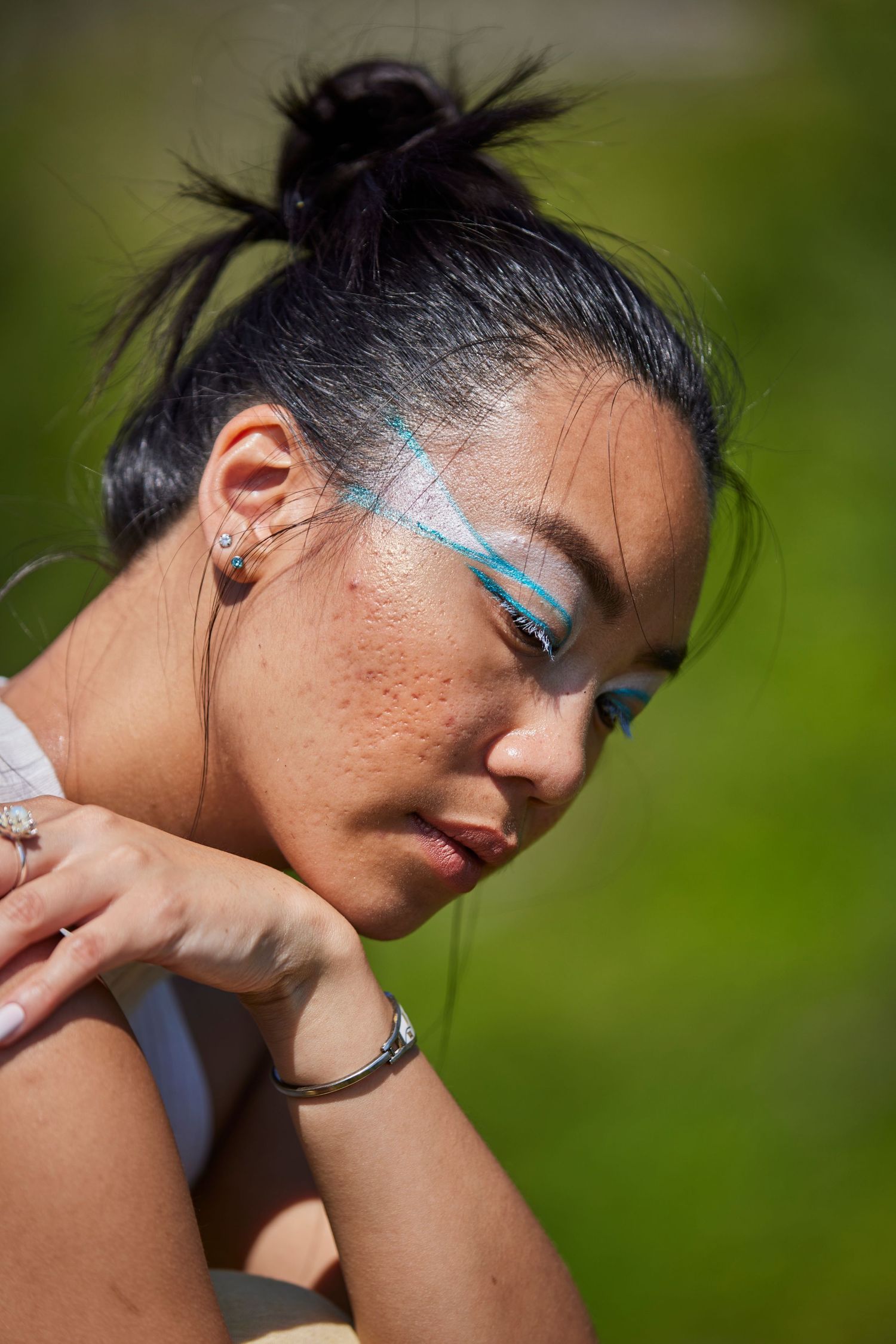 Portrait featuring sparkly blue face paint and a messy bun hairstyle against a green background.