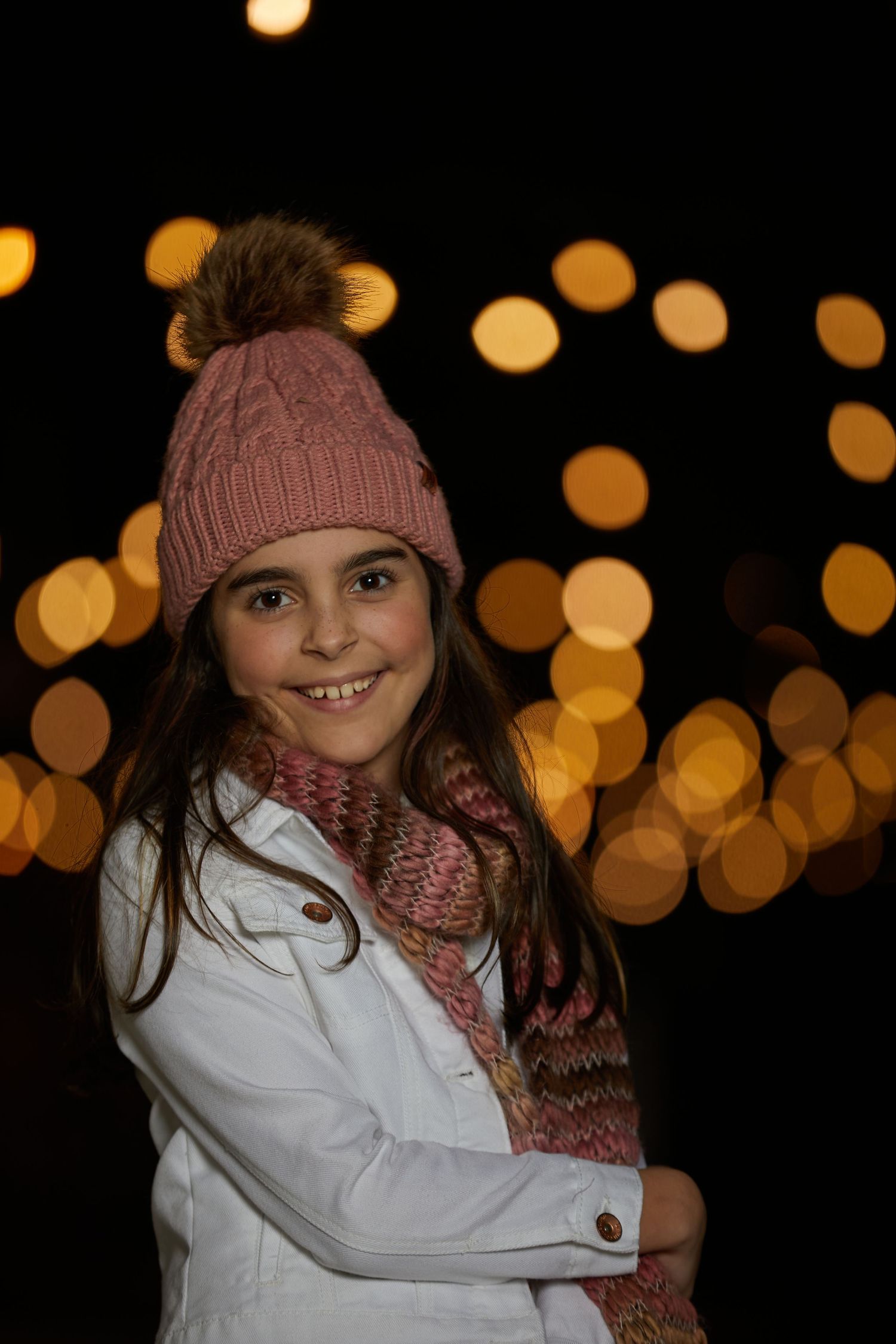 Winter portrait with bokeh lights featuring a cozy knit hat and scarf against dark background.