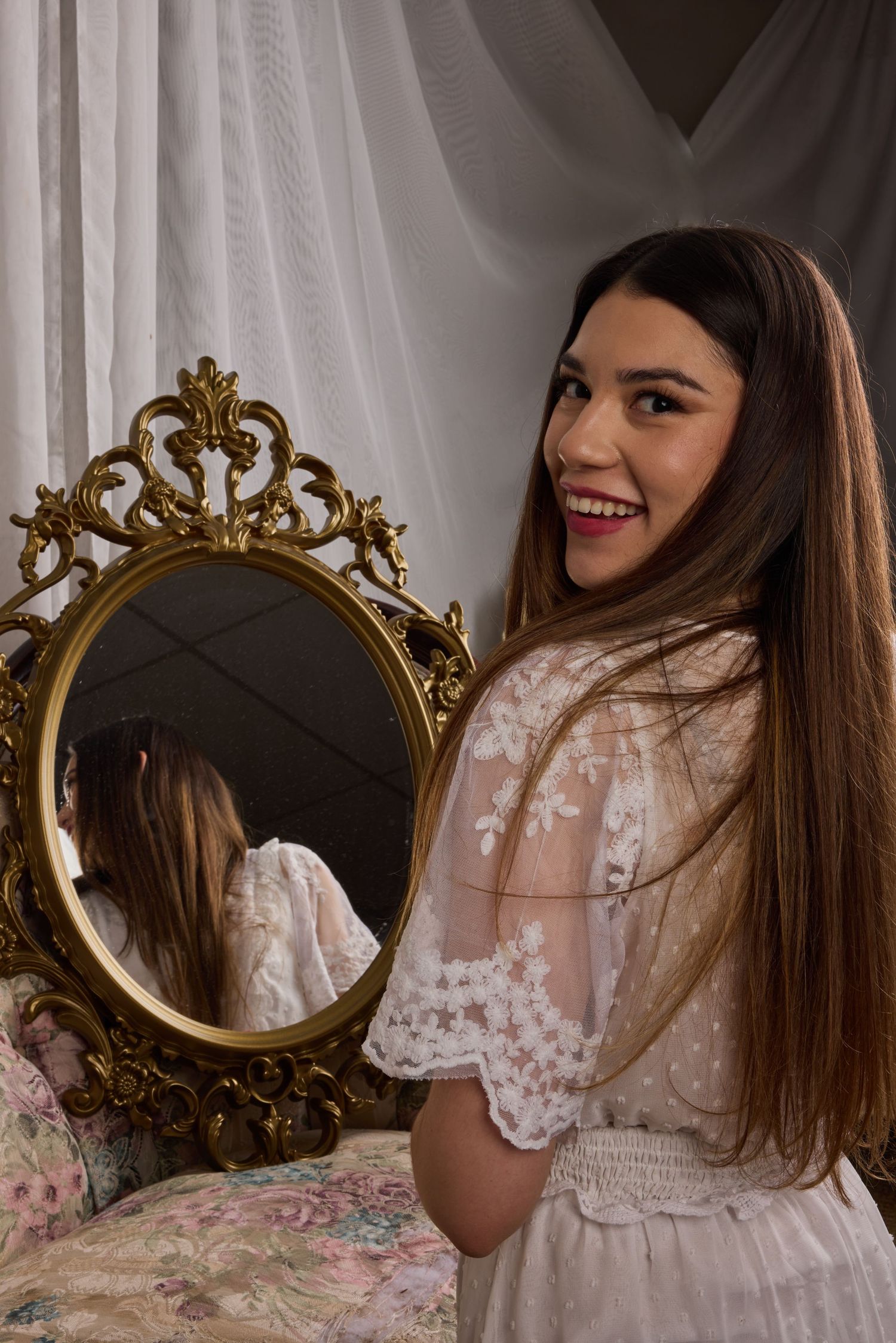 Vintage-inspired portrait with ornate gold mirror and white lace dress in romantic boudoir setting.