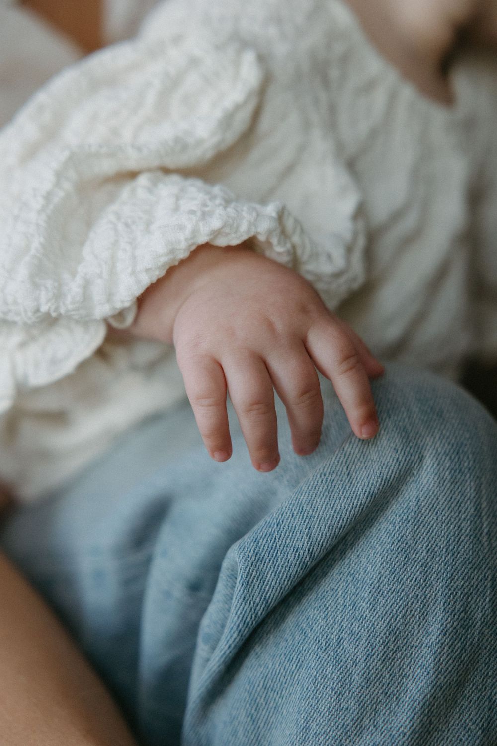 Close-up detail of small baby hand resting on denim fabric.