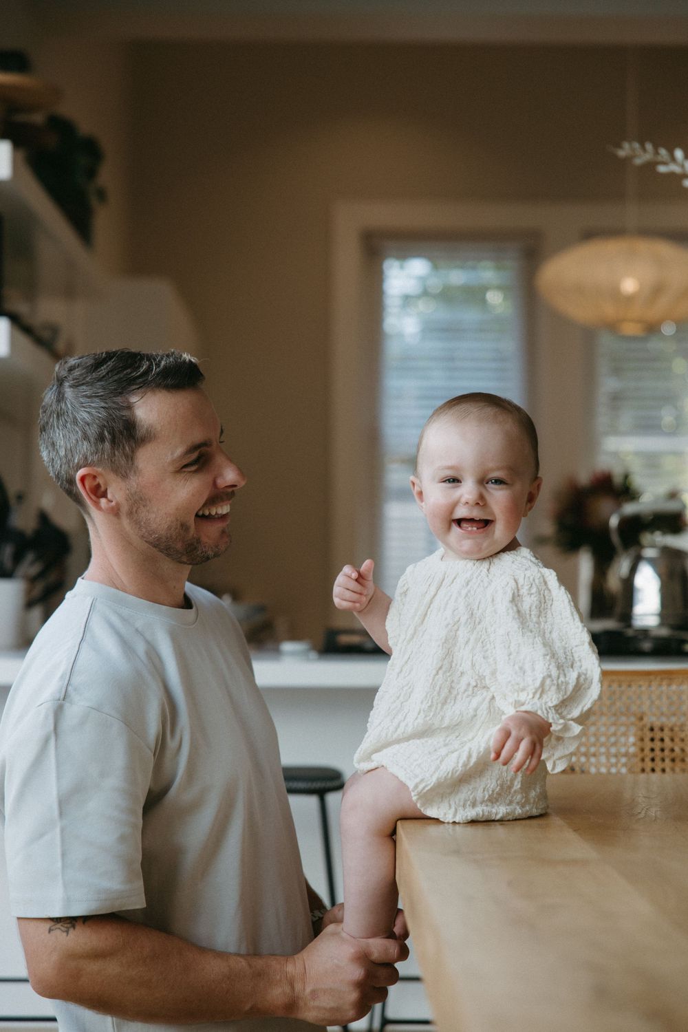 A series of candid photos showing joyful moments between parent and baby in a warm, sunlit kitchen.