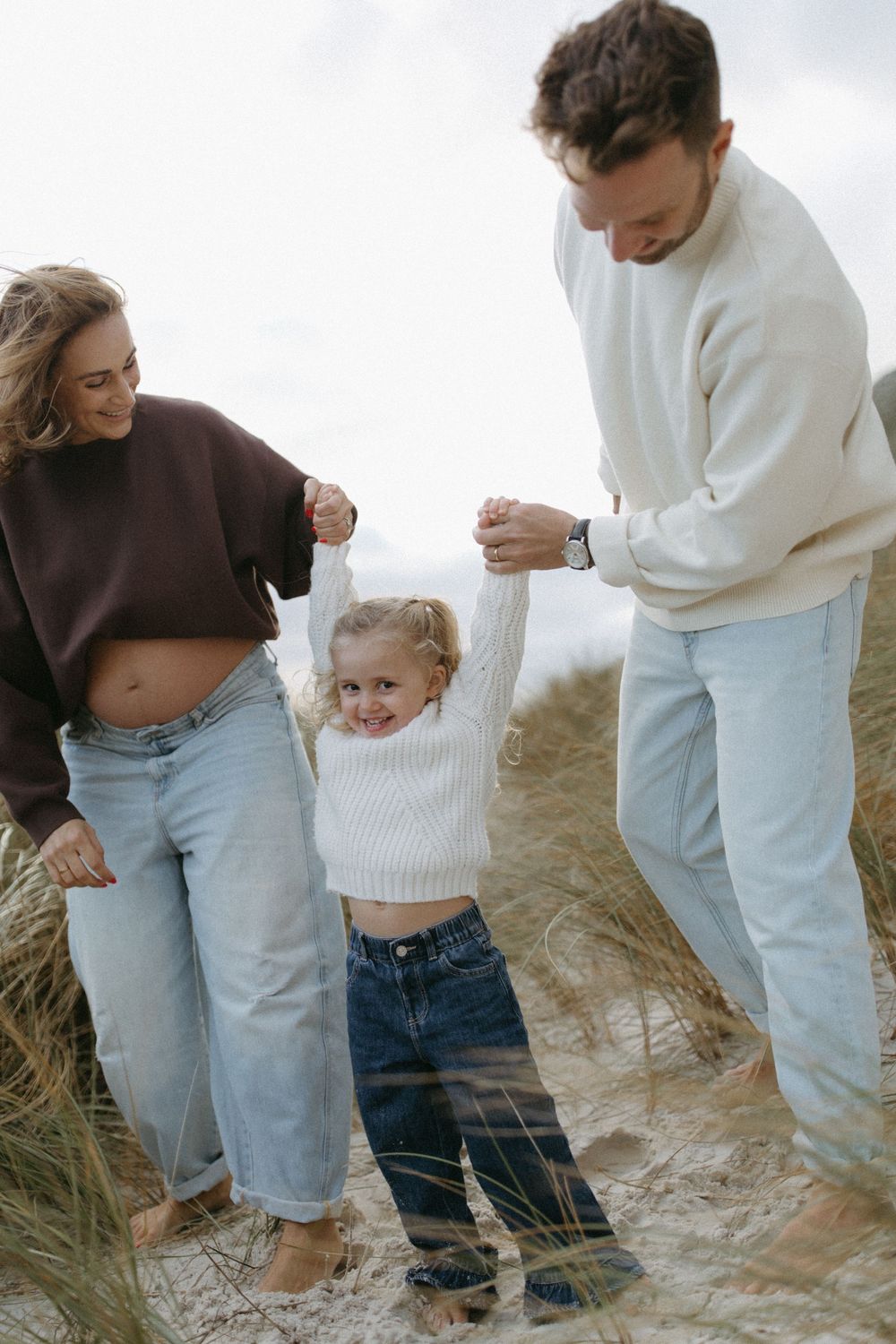 A family plays together on sandy dunes wearing coordinated casual outfits.