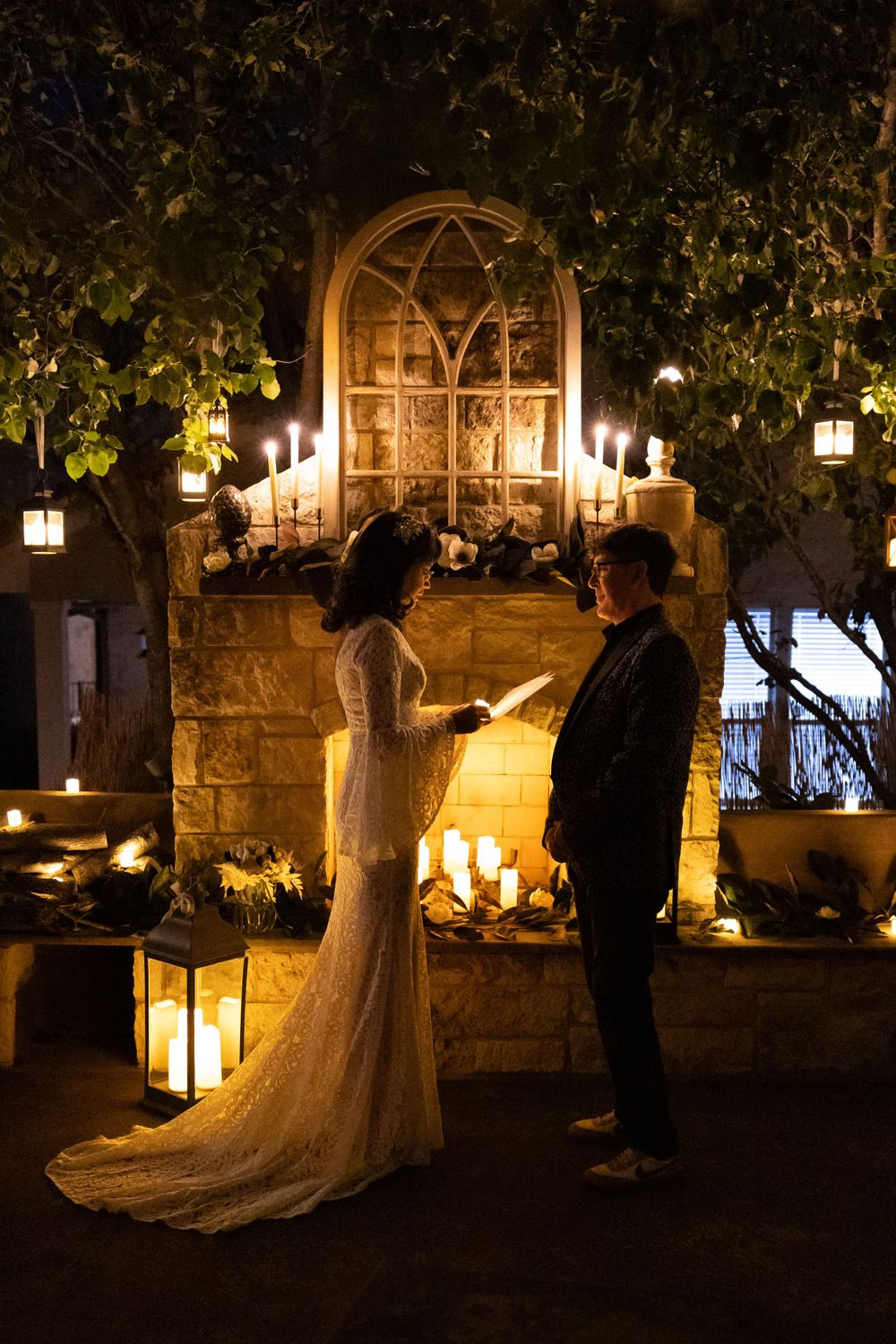 A romantic wedding scene at night with candlelight and lanterns illuminating a couple in an outdoor garden setting.