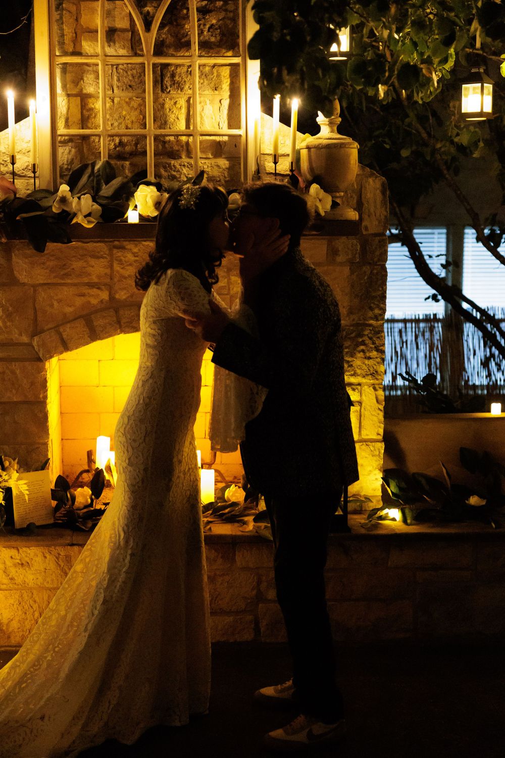 Silhouettes of a wedding couple standing close in candlelit garden setting.