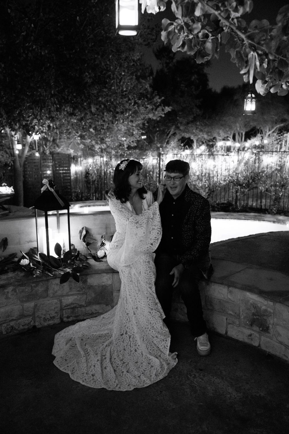 A black and white portrait of newlyweds in an enchanted garden setting with hanging lanterns.