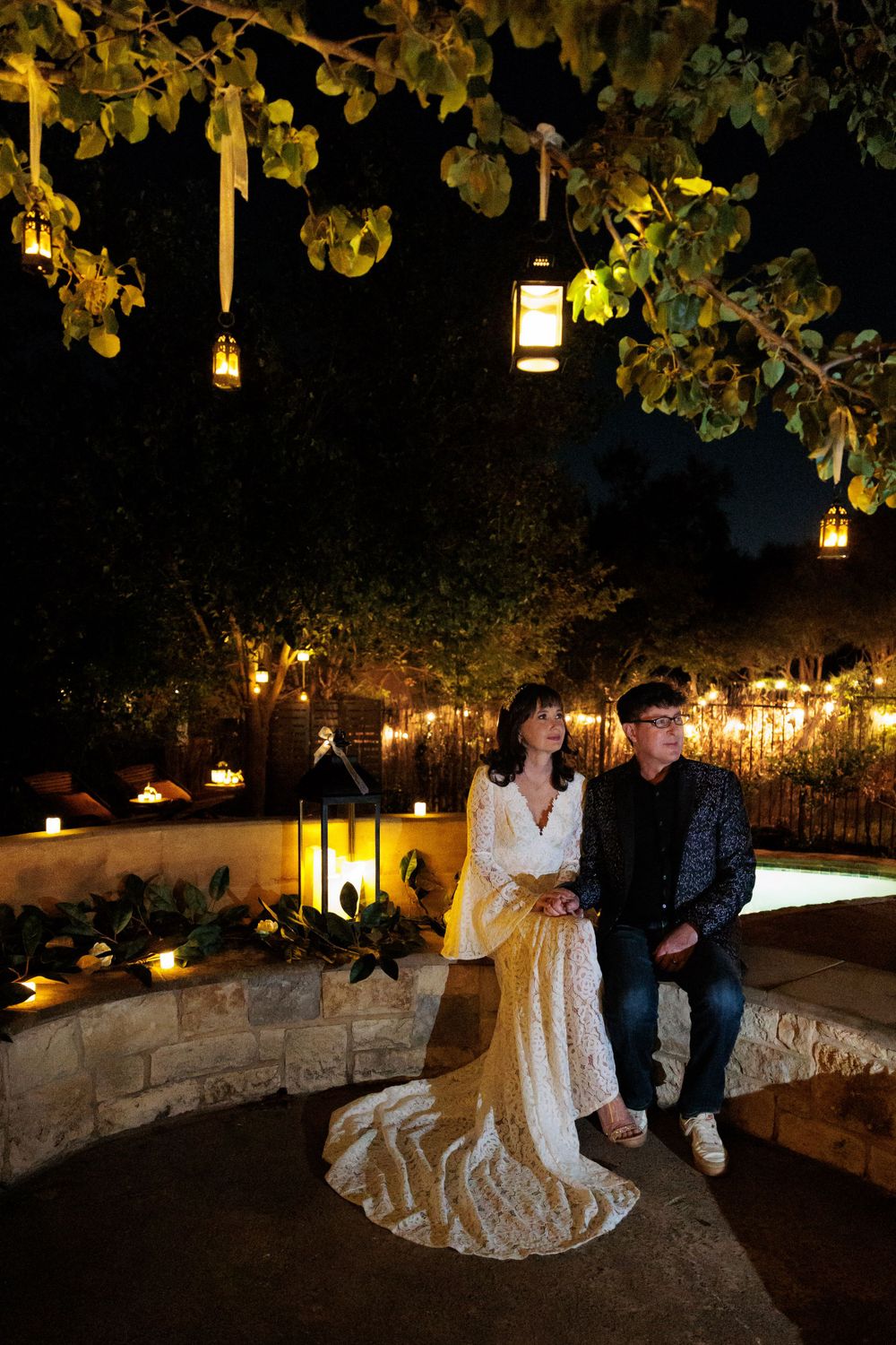 A couple poses in an outdoor garden setting with hanging lanterns creating a romantic ambiance.