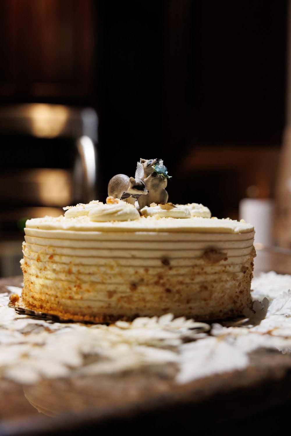A white wedding cake decorated with small figurine toppers sits on a rustic surface.