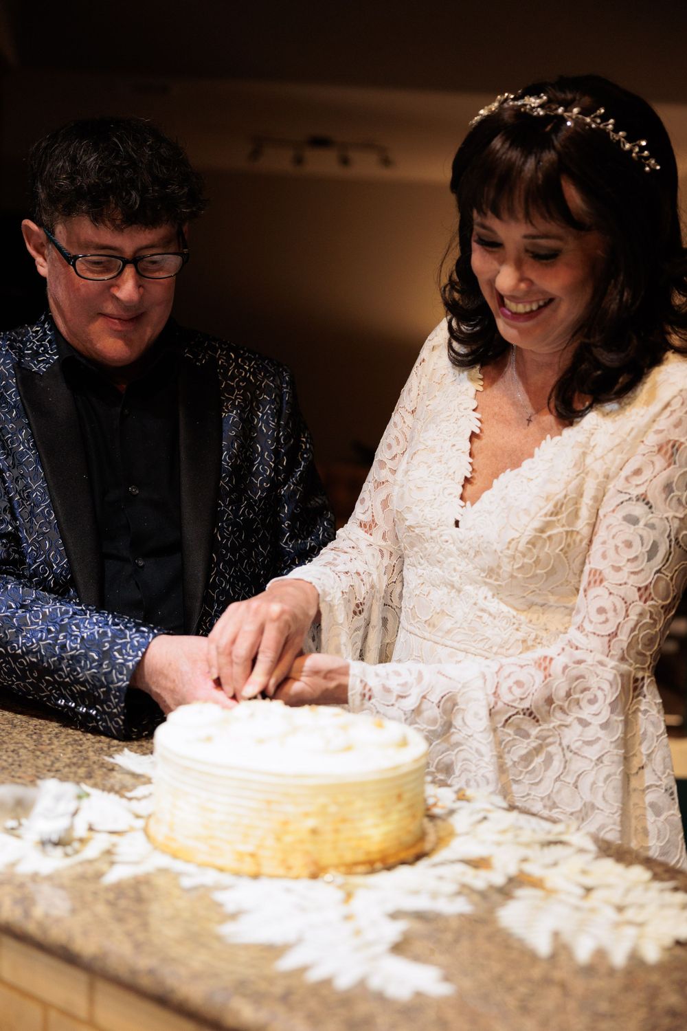 A couple cuts their wedding cake together while dressed in formal attire.