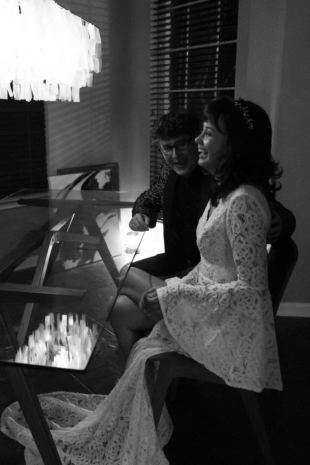 Black and white photo of couple at desk in formal attire with window light streaming in.