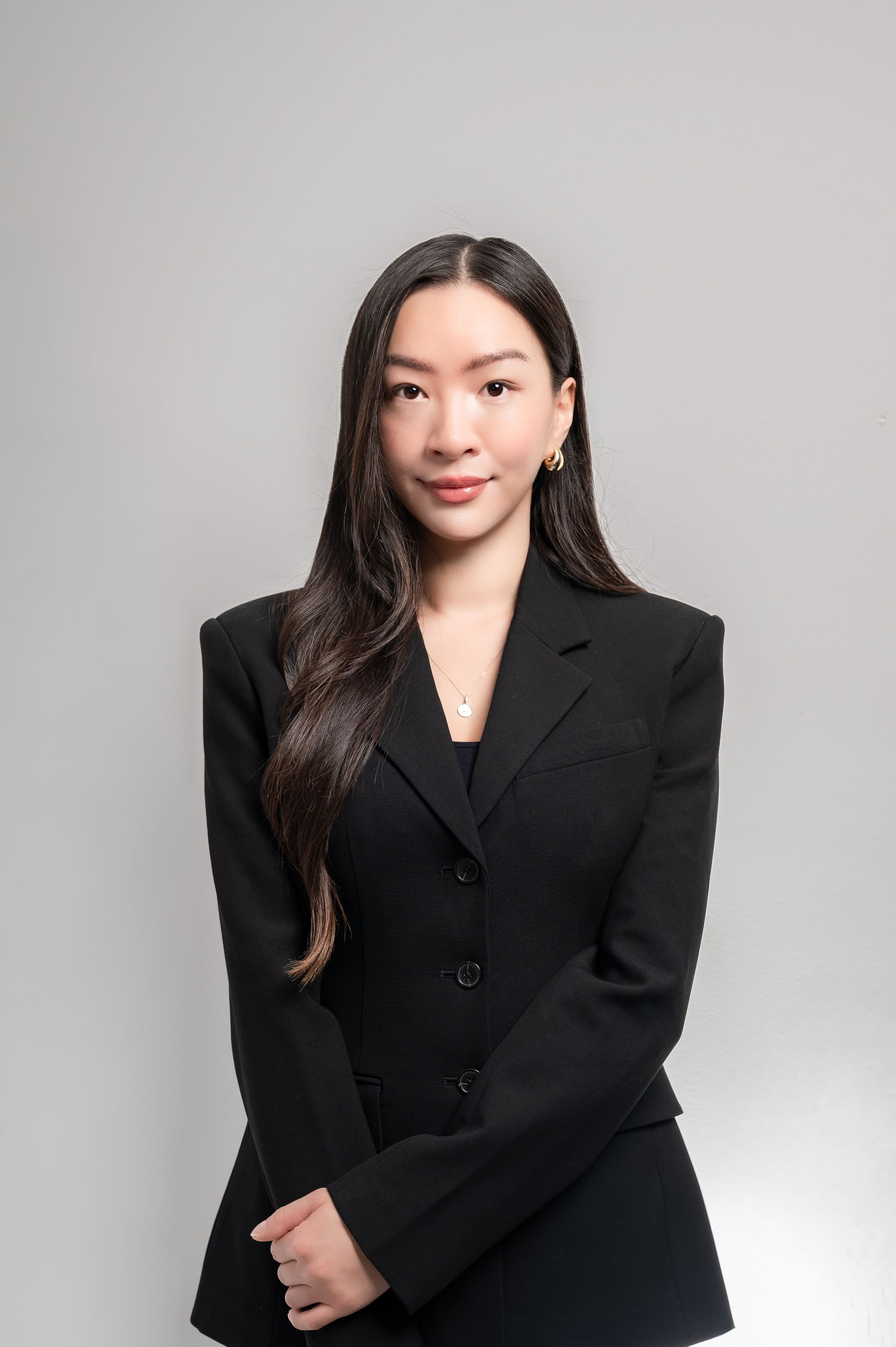 Professional woman in black blazer posing for a corporate headshot against a light gray background.
