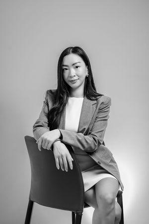 Black and white portrait of a professional woman in blazer seated on chair, exuding confidence.