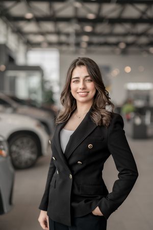 Professional woman in black blazer smiling confidently in a modern car dealership showroom.