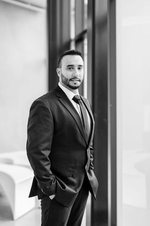 Professional man in dark suit and tie posing confidently in a modern office, black and white portrait photo.