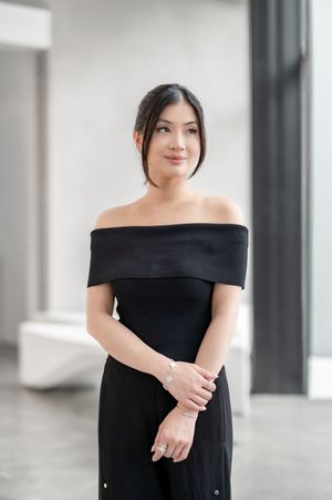 Woman in black off-shoulder dress posing indoors, wearing bracelet and ring, with elegant minimalist style.