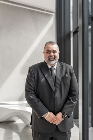 Professional man in dark suit and tie smiling confidently in a modern building interior.