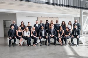 Professional corporate team in black attire posing for a group photo in a modern white office space.
