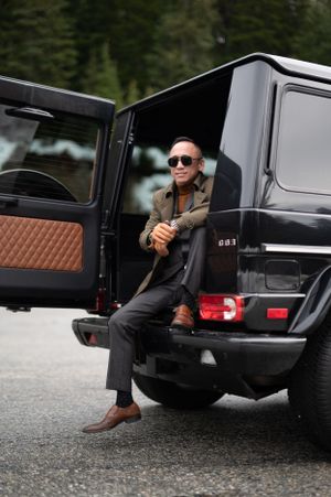 A stylish passenger sits in a black Mercedes G-Wagon with custom brown leather interior parked on a mountain road.
