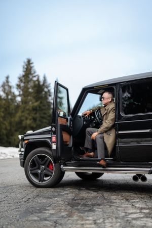 Luxury black Mercedes G-Wagon parked on snowy mountain road with open door in winter setting.