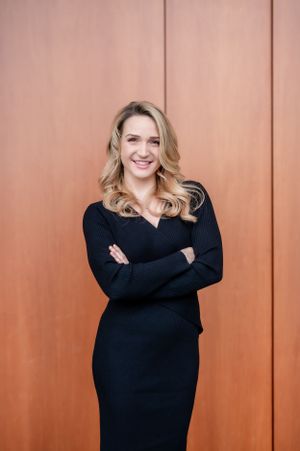 Professional portrait in black dress standing with arms crossed against terracotta colored wall.