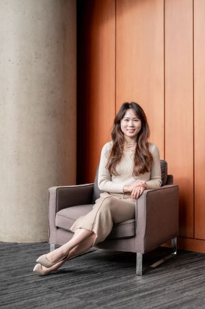A woman in neutral tones sits elegantly in a modern armchair against a terracotta wall and concrete column.
