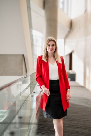 Professional woman in modern office building wearing a striking red blazer over white top and black skirt.