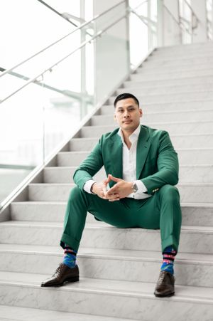 Professional sitting on modern stairs wearing vibrant green suit with colorful striped socks and brown dress shoes.