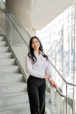 Professional wearing a crisp white button-down shirt and black pants poses confidently on marble stairs in bright setting.