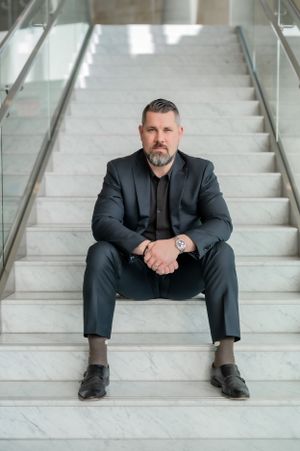 Business professional in dark suit sits contemplatively on marble steps in modern building interior.