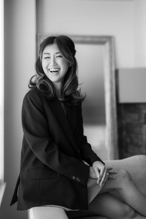 Black and white portrait of someone laughing joyfully while wearing a dark blazer in a casual indoor setting.