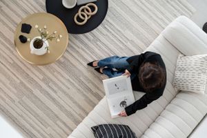 Overhead view of someone working on laptop from white couch with round coffee table and decorative pillows nearby.