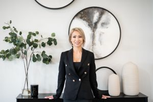 Professional business portrait in front of white wall with circular art and eucalyptus plant decor.