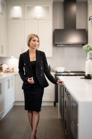 Professional in a black business suit standing in modern white kitchen with dark countertops and stainless appliances.