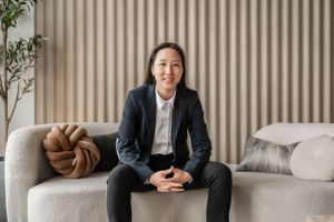 A professional in a navy blazer and white shirt sits comfortably on a modern gray couch with decorative pillows.