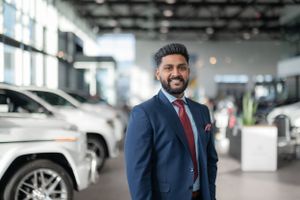 Professional in navy suit smiling in luxury car dealership showroom.