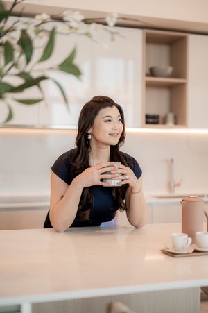 Woman in navy blue top sits at minimalist cafe table holding beverage cup while gazing to the side.