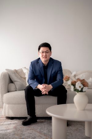 A person in a navy blazer sits on a light gray couch with a white vase on a nearby table.