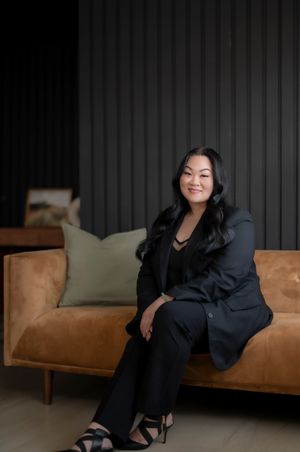 Professional seated on a tan leather couch wearing black business attire in a modern interior setting.