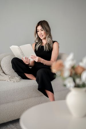 Person in all black relaxing on a light gray couch while reading a book in a minimal modern living room setting.