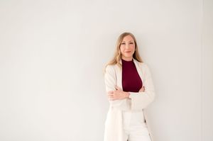 Professional wearing a burgundy turtleneck and cream blazer poses against a white background.