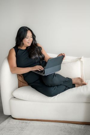 Person relaxing on white couch while working on laptop tablet in comfortable dark outfit.