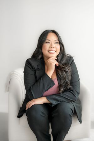 A person in a black business suit sits casually on a white couch while laughing and expressing joy in four poses.