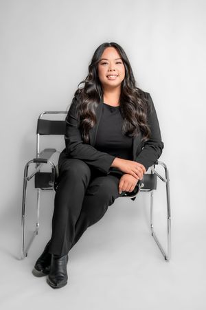 A person in all black lounges on a modern chrome chair against a white backdrop in a stylish photoshoot.