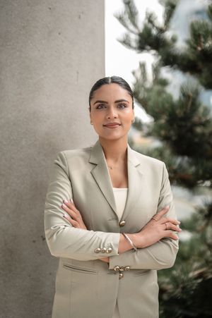 Professional wearing a light beige blazer stands confidently with arms crossed against a neutral background.