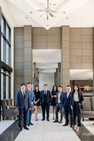 Eight business professionals in suits pose in a modern corporate lobby with high ceilings and elegant decor.