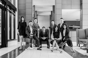 Black and white professional group photo of eight business professionals posed in a modern corporate lobby.
