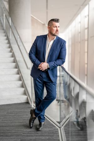 Professional in a navy suit poses confidently against a modern office stairwell in a series of dramatic shots.
