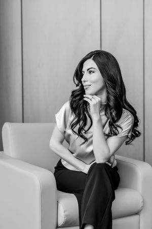 A black and white portrait series showing a person in a black outfit posing thoughtfully on a light colored chair.
