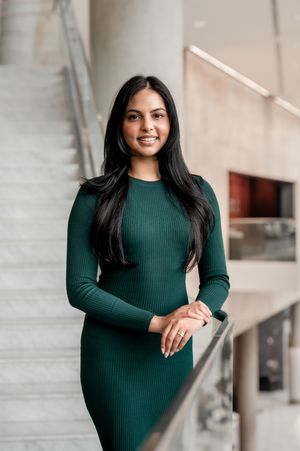 Professional portrait of someone in an elegant emerald green ribbed dress standing in a modern office setting.