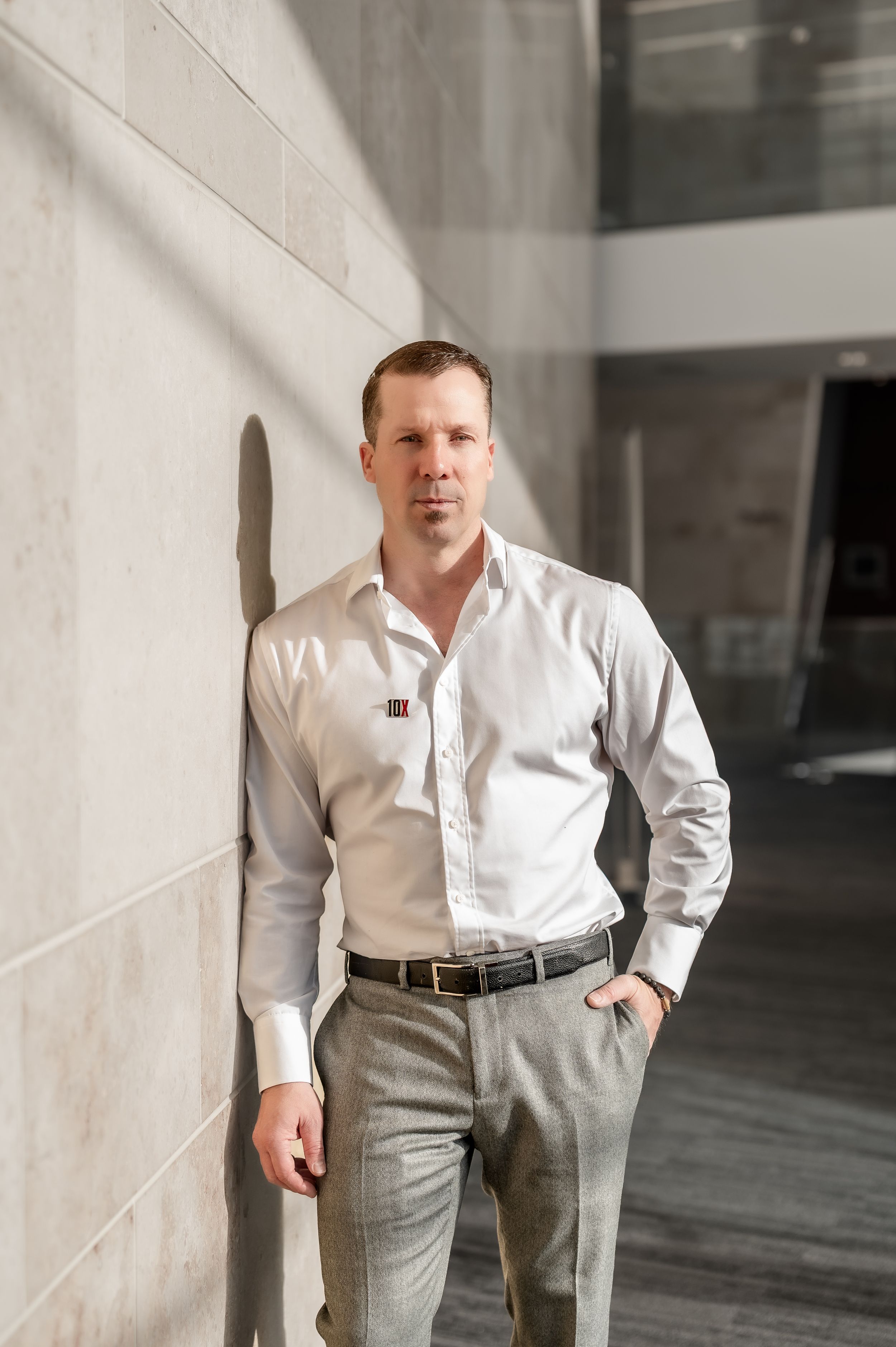 A person in a white dress shirt and gray pants poses in different stances against a light-colored wall.
