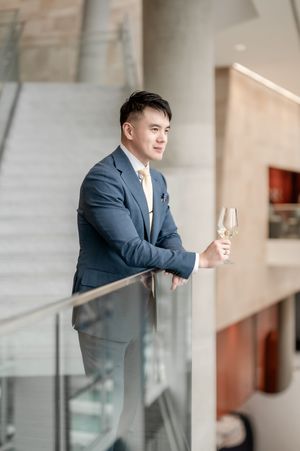 A businessman in a navy suit stands at a glass railing in a modern office building hallway.